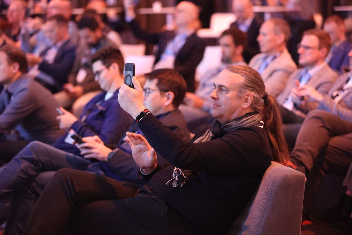 Konferenzteilnehmer fotografiert begeistert die Bühne während einer Keynote von Dr. Jonathan Mall